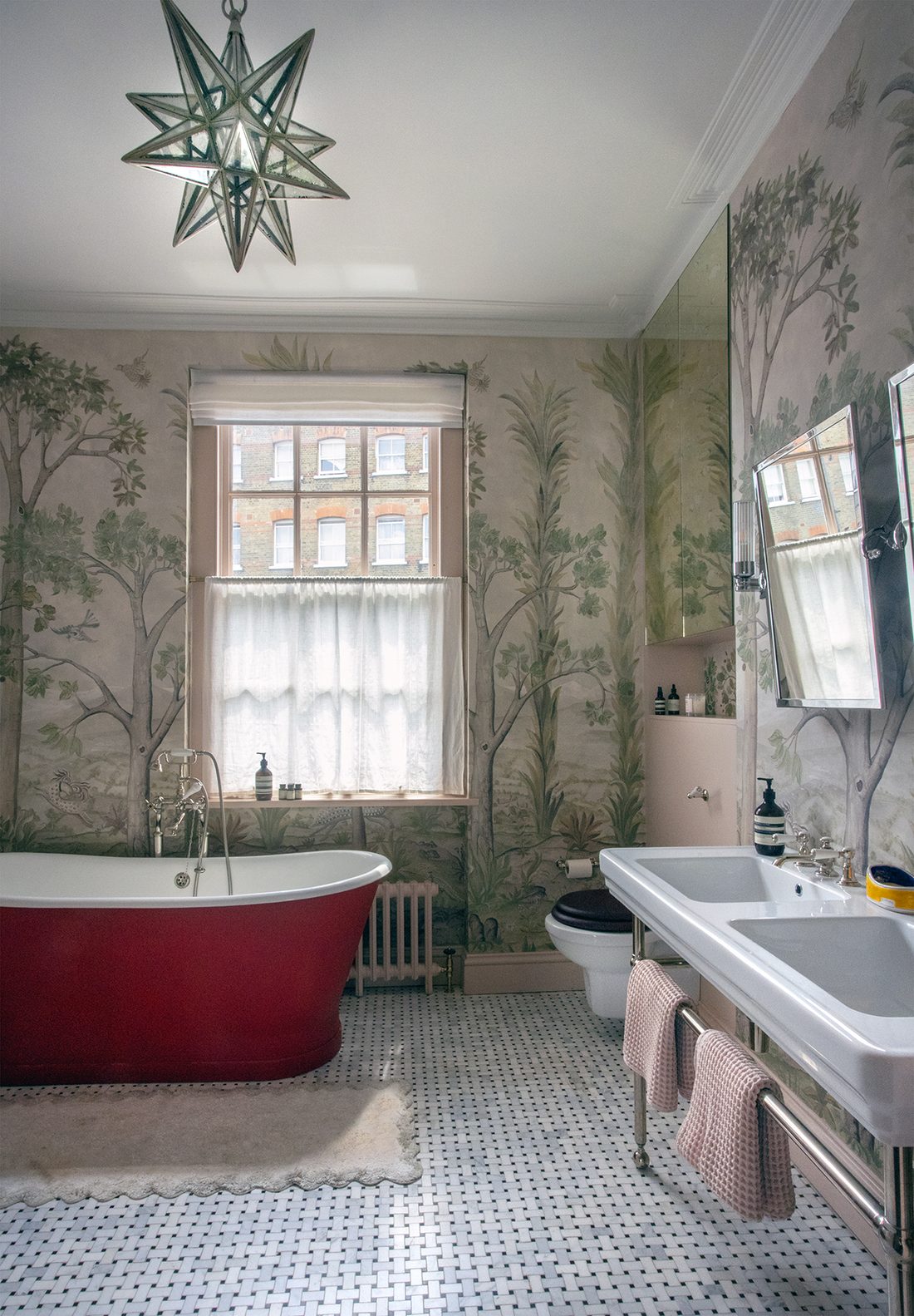 Bathroom with a red roll-top bath, hand-painted tree mural, star pendant and basketweave marble floor, designed by Make My House Home